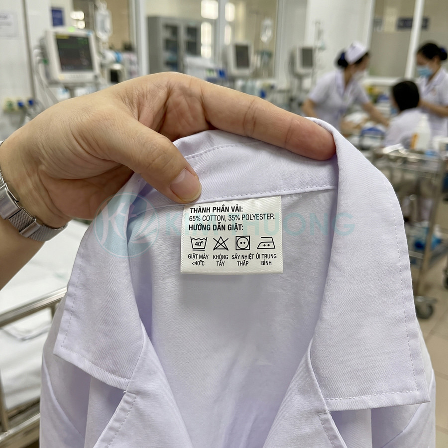 Áo blouse trắng với nhãn thành phần 65% cotton, 35% polyester và hướng dẫn giặt ủi tiếng Việt